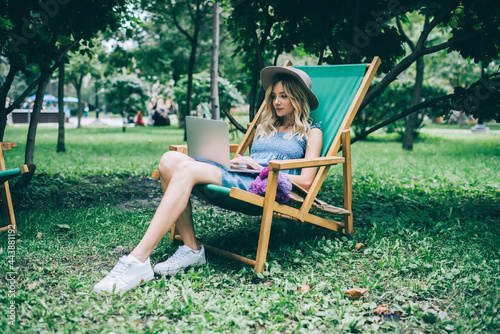 Caucasian digital nomad with violet flowers checking information about floristic delivery on laptop website using 4g wireless in park, millennial female graphic designer doing distance job on netbook