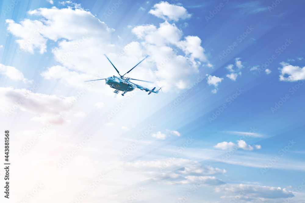 A helicopter flies high in the blue sky, in the rays of the sun and clouds. Rescue operation. Military equipment transport. A helicopter flies high in the blue sky, in the rays of the sun and clouds. Rescue operation. Military equipment transport.
