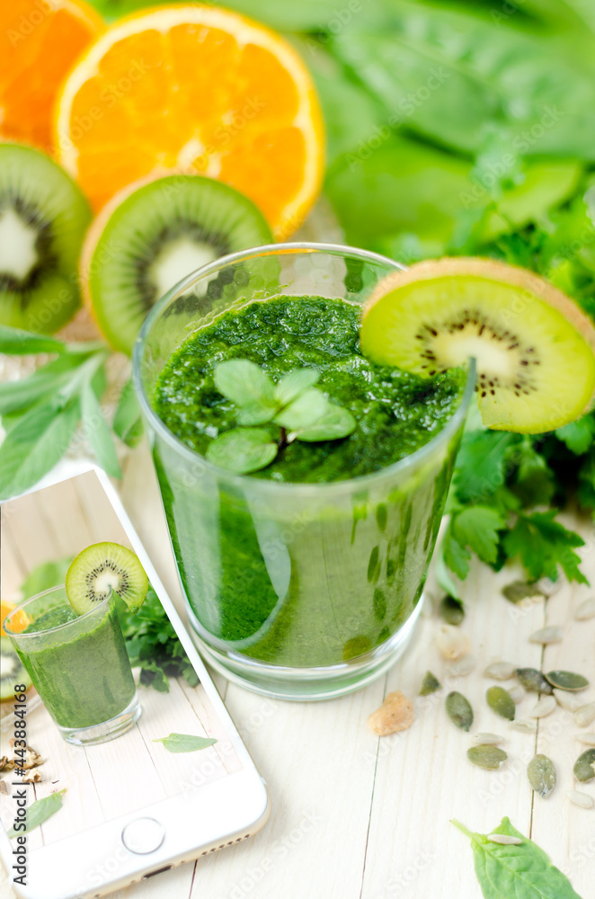 Healthy green smoothie with spinach, kiwi and orange and mobile phone with image on wooden light retro table. Healthy green smoothie with spinach, kiwi and orange and mobile phone with image on wooden light retro table.