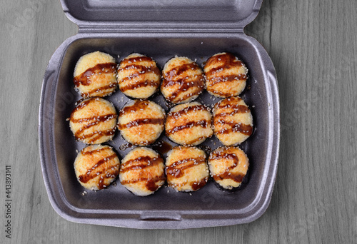 A set of baked sushi in a plastic container, prepared for delivery. On a wooden background, top view.