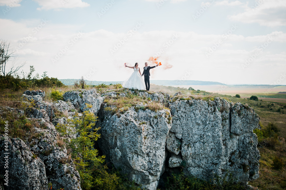 Newlyweds stand against the background of rocks and hold colorful smoke in their hands Newlyweds stand against the background of rocks and hold colorful smoke in their hands