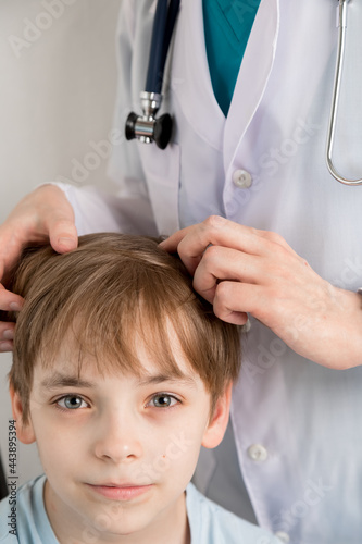 The child's head is examined by a medical professional wearing gloves for lice in his hair. Pediculosis disease