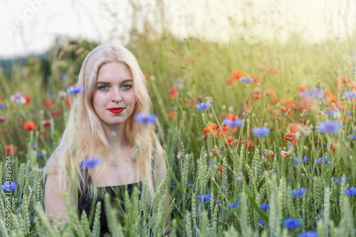 Atractive young woman is posing in a cereal field with red poppies and blue cornflowers. Horizontally. 