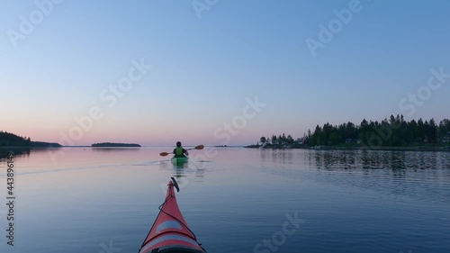 Girl kayaking and then taking break from paddling, mirror like calm water at midnight in Northern Sweden during light Summer night Sun in polar regions. Umea, Sweden.
