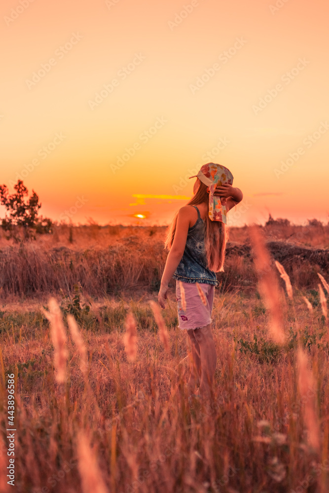 A girl stands in a field and looks at the sunset. Summer vacations and rest in the village