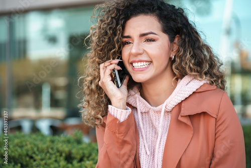 Latin woman smiling while talking on the phone outdoors in the street.