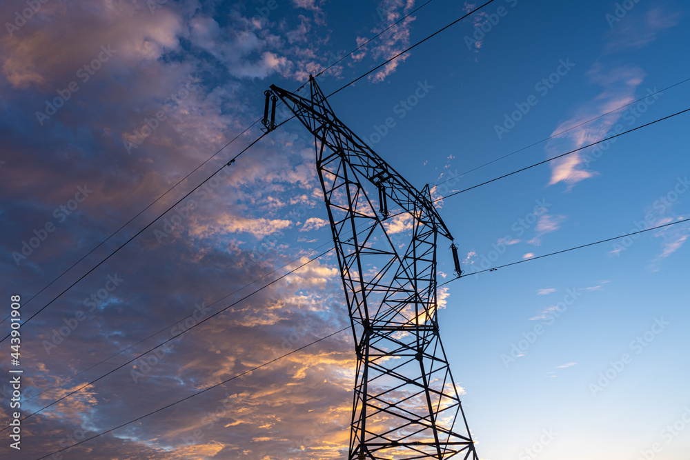 High voltage electrical tower, with the light of dawn, and a beautiful cloudy sky.
