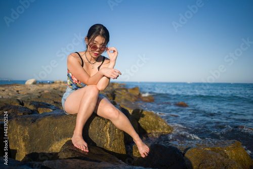 young Asian woman by blue sea - happy and beautiful Chinese girl enjoying holiday trip relaxed and cheerful at beach rock cliff during summer in tourist travel concept
