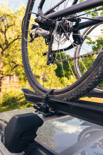 Bicycle installed to roof bike rack on a silver car, coutryside landscape in background