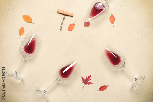 Fototapeta Naklejka Na Ścianę i Meble -  Flat lay of red wine in glasses with corkscrew and autumn leaves on beige concrete grunge background. Top view.
