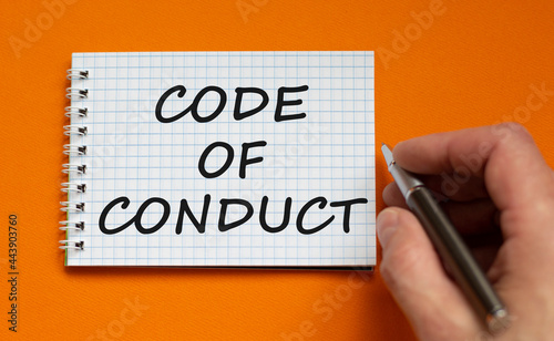 Code of conduct symbol. Businessman writing words 'Code of conduct' on white note. Beautiful orange background. Business and code of conduct concept. Copy space.