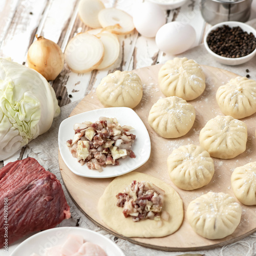 Dumplings stuffed with minced meat and cabbage. Convenience Food. Cooking process. Slices of raw dough with filling on wooden cutting board. Top view. Square format. Soft focus.