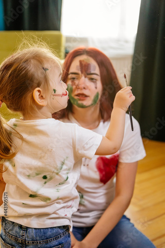 Family hobbies leisure activity home concept. Mother and small daughter drawing with fun using paintbrushes and watercolors. Children and parent creating picture together, body paint, home quarantine.