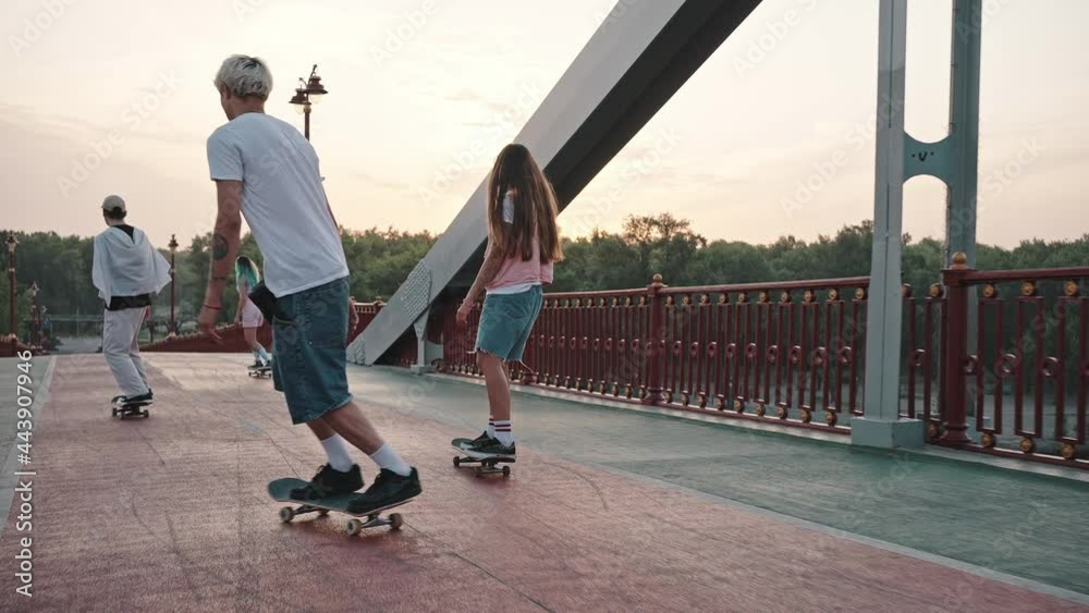 Group of skaters, boys and girls, ride their skateboards across the large city bridge at dawn. Youth culture and freedom of expression concept