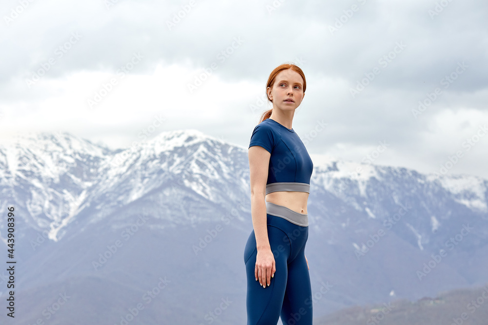 Determined woman have rest after workout outdoors, stands looking at side, after running, enjoy free time, relax, in contemplation. Mountains in the background