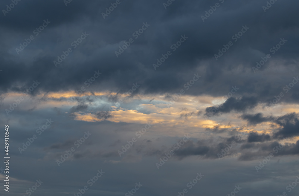 Dark dramatic clouds and sunny areas of the sunset sky in summer.