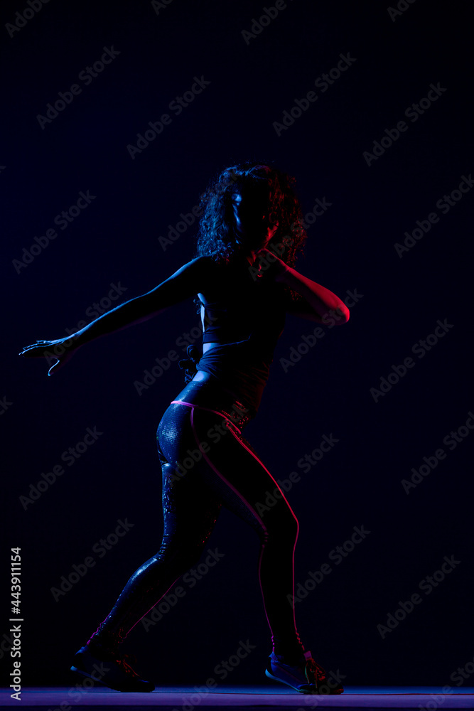 Silhouette of a girl dancing zumba. Side lit with blue and red lights on dark background.