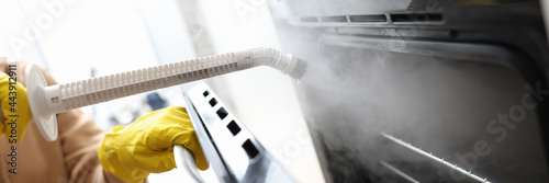 Woman in protective gloves washing oven with steam brush closeup