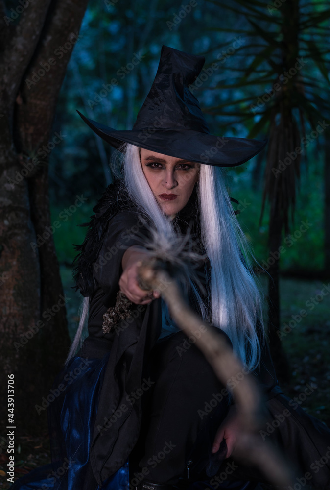 Woman in a witch costume in the forest at twilight holding a wooden stick Woman in a witch costume in the forest at twilight holding a wooden stick