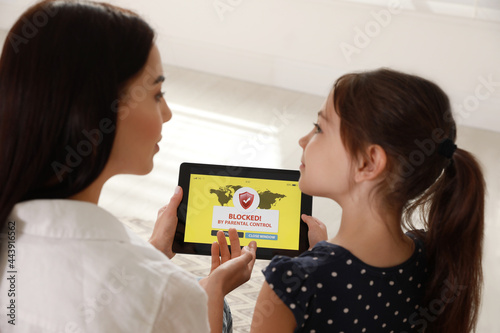 Mother using parental control app on tablet to ensure her child's safety at home photo