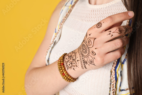 Woman with beautiful henna tattoo on hand against yellow background, closeup. Traditional mehndi photo