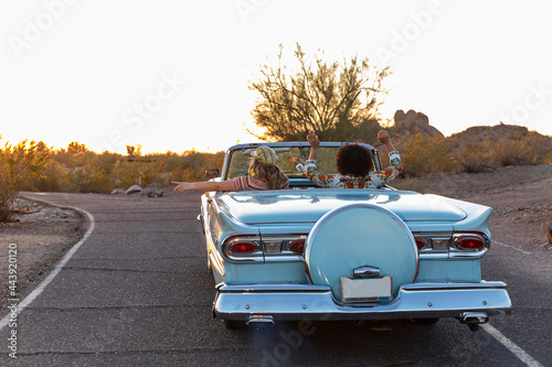 Two Best Girlfriends Girls on Desert Road trip driving down road in classic car  photo