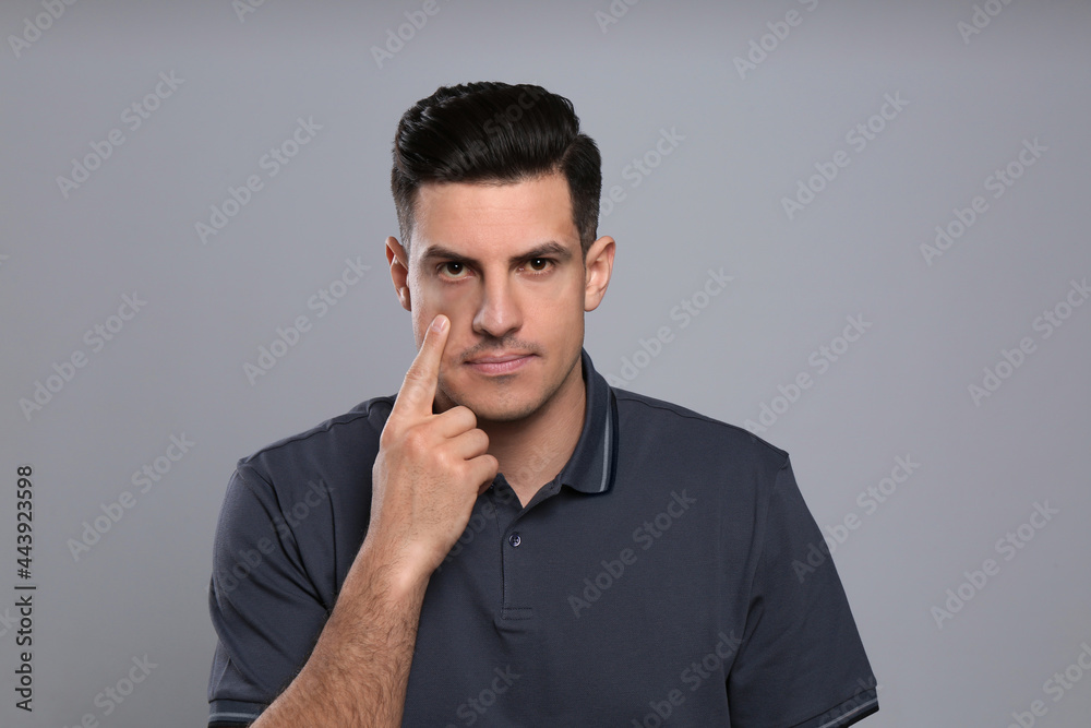 Man checking his health condition on grey background. Yellow eyes as symptom of problems with liver Man checking his health condition on grey background. Yellow eyes as symptom of problems with liver