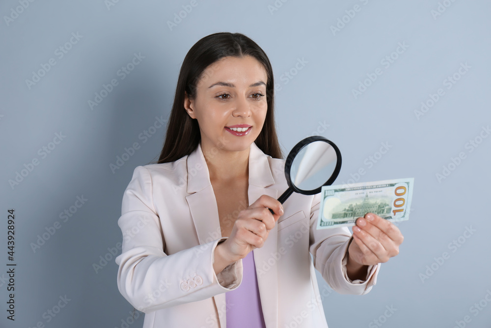 Expert authenticating 100 dollar banknote with magnifying glass on light grey background. Fake money concept Expert authenticating 100 dollar banknote with magnifying glass on light grey background. Fake money concept