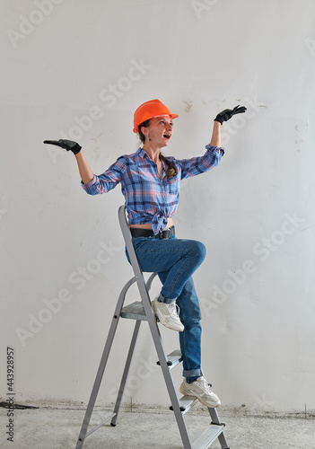 a cheerful builder in a helmet sits on a stepladder