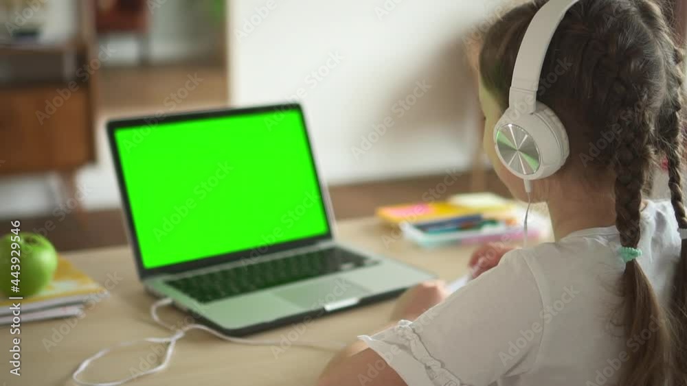 Child in headphones look at laptop green screen and talk on video call lesson at home Spbd. Webcam