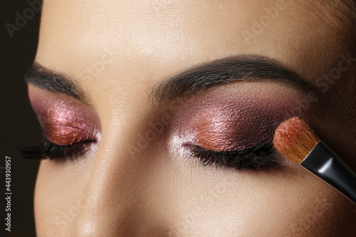 Applying dark eye shadow with brush onto woman's face, closeup Fototapeta