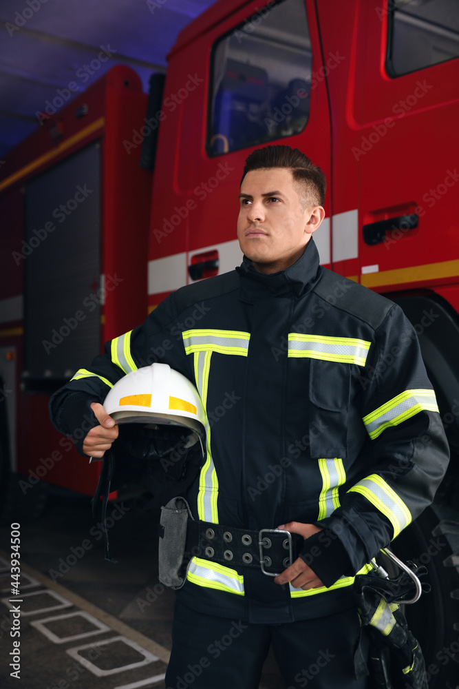 Portrait of firefighter in uniform with helmet near fire truck at station Portrait of firefighter in uniform with helmet near fire truck at station