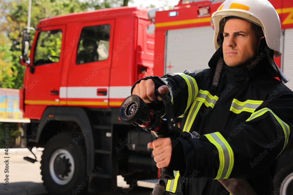 Fototapeta premium Firefighter in uniform with high pressure water jet near fire truck outdoors