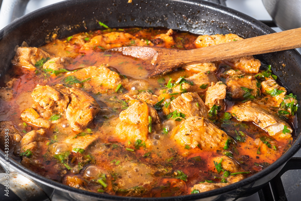 Homemade chicken curry is cooked in a skillet. Chicken pieces are cooked in red sauce with butter and chopped cilantro, close-up Homemade chicken curry is cooked in a skillet. Chicken pieces are cooked in red sauce with butter and chopped cilantro, close-up