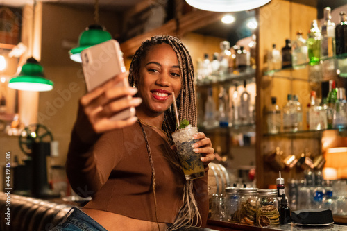 Trendy black female taking selfie in bar photo