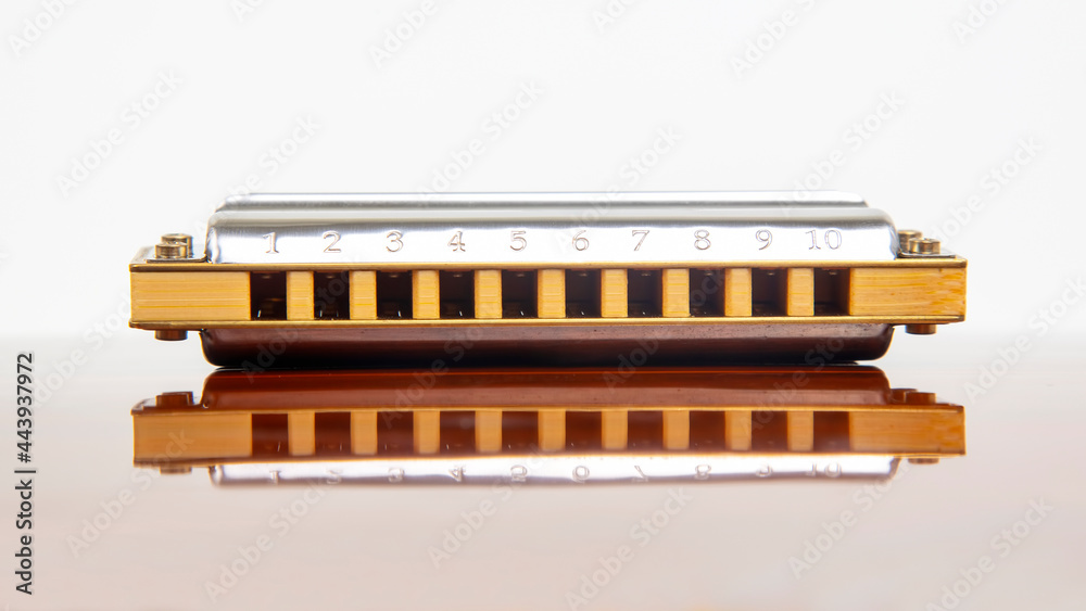 The harmonica lies on a mirrored surface. Classical musical wind instrument. The harmonica lies on a mirrored surface. Classical musical wind instrument.