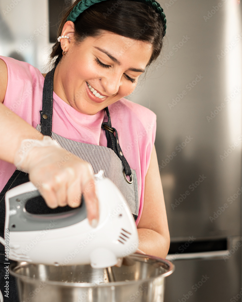 Young smiling woman churning buttercream in a metal bowl Young smiling woman churning buttercream in a metal bowl