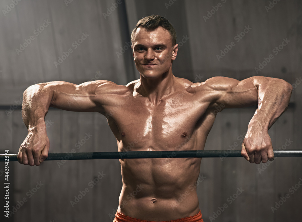 Smiling male athlete doing pull ups on bar during cross fit training in gym
