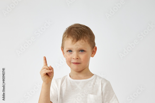 Portrait of a boy with a funny face and a white T shirt pointing up on a white background