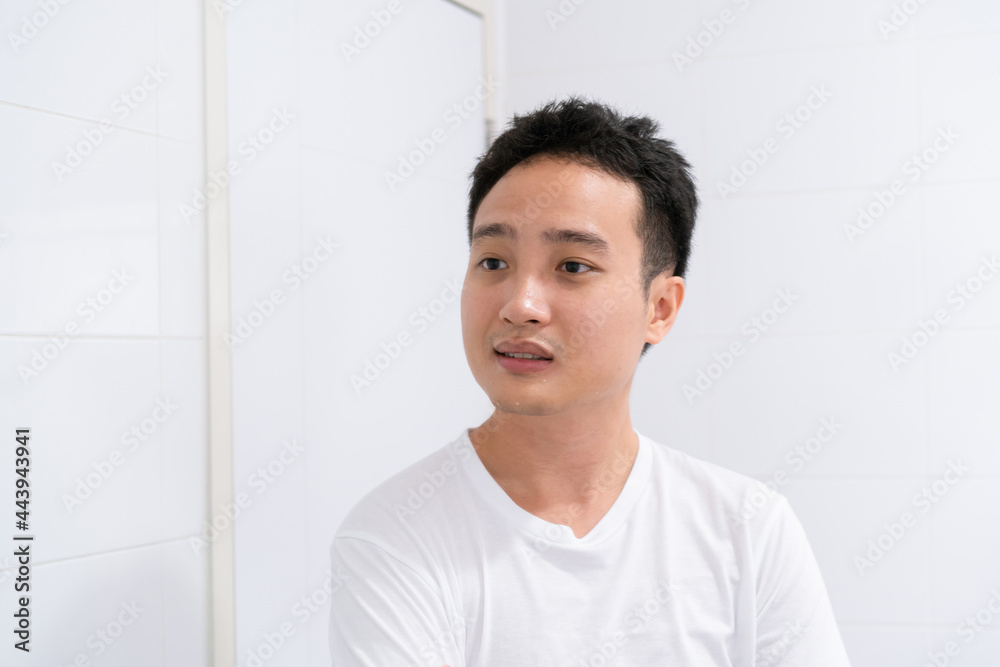 Cheerful Asian young man looking himself in the mirror in bathroom after washing his face. Cheerful Asian young man looking himself in the mirror in bathroom after washing his face.