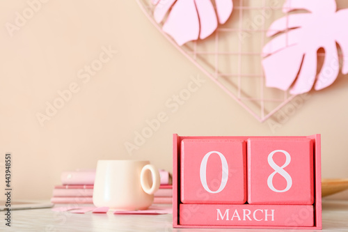 Cube calendar with date MARCH 8 and cup on table in room, closeup