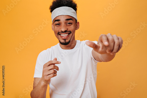 Fototapeta Stylish man in white T-shirt laughs and points his finger at camera