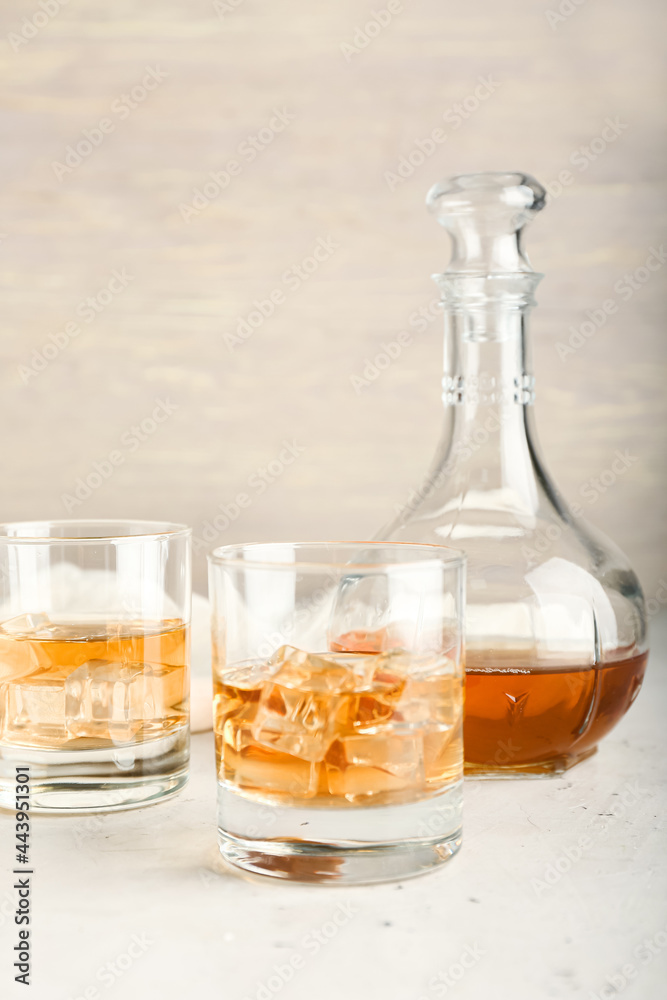 Jug and glasses of cold whiskey on light background