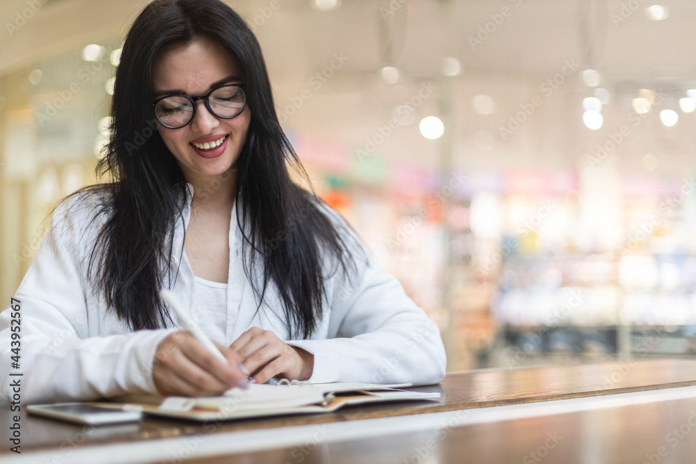 Happy Asian young woman sitting at cafe with coffee cup taking notes enjoying break