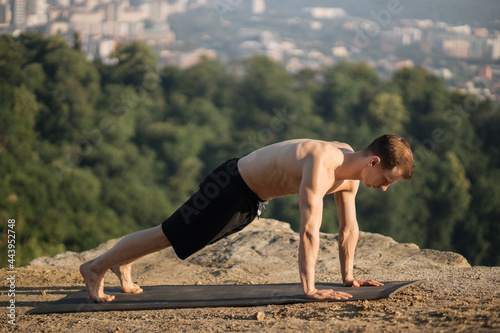 Caucasian athlete with muscular bare torso standing in plank position on yoga mat on fresh air. Young healthy man training abdominal muscles outdoors.