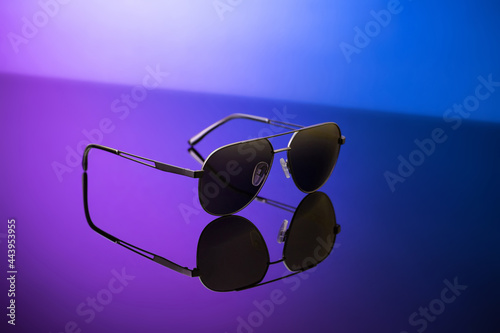 Black sunglasses on blue reflective surface, closeup. Product photography and fashion concept