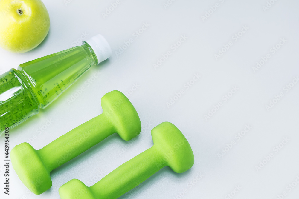 Fototapeta premium Dumbbells, fresh fruit apple and multivitamin juice on light grey surface with copy space. Healthy sport and diet concept.