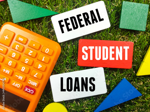 Colorful wooden board with calculator and text FEDERAL STUDENT LOANS on grass background. photo