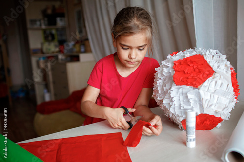 Preteen girl doing pinata with cardboard from used box and color crepe paper, decorated container filled with candy as a part of celebration, diy decoration at birthday, soccer party