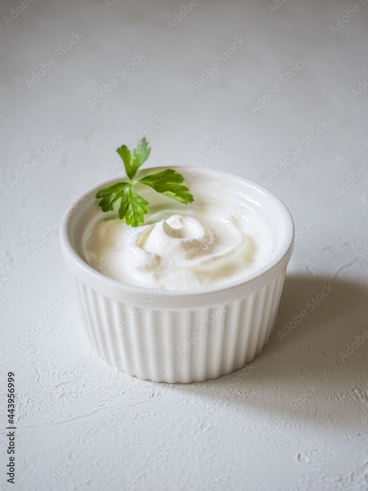 Close-up of fresh sour cream in white sauce bowl. Whirlpool of sour cream. Parsley leaves for decoration. Light concrete background. Delicious and natural dairy product Close-up of fresh sour cream in white sauce bowl. Whirlpool of sour cream. Parsley leaves for decoration. Light concrete background. Delicious and natural dairy product